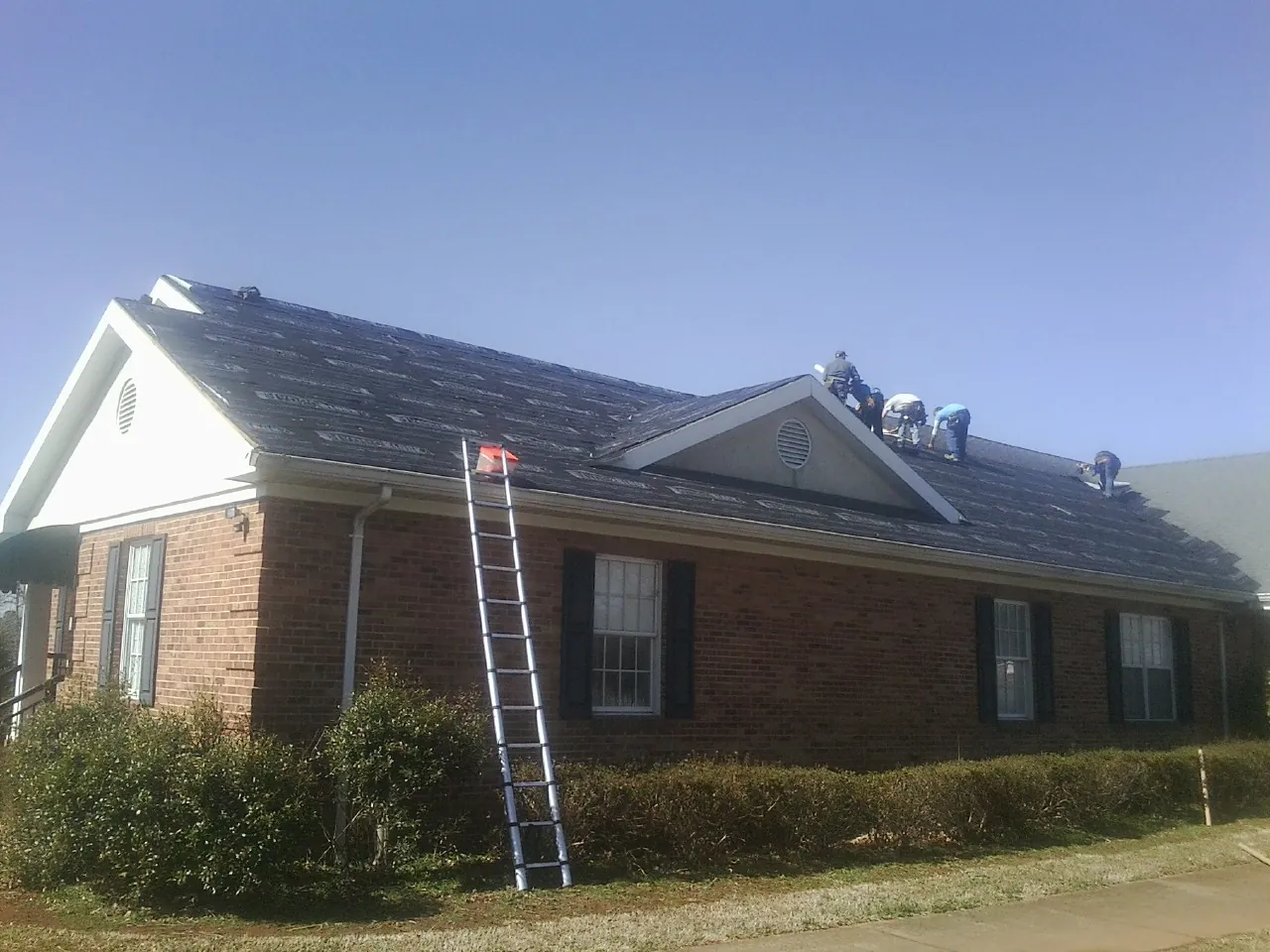 Crew tearing shingles off a brick ranch roof with a ladder set — Emergency Roof Repair work by our crew in Showell