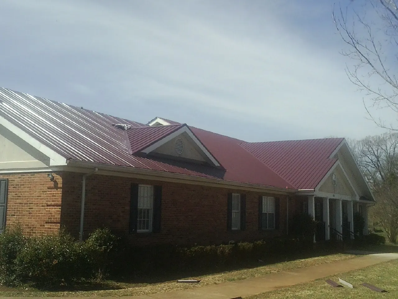Red metal roof with gabled entries on a long brick building, from a Hail Damage Roof Repair job in Showell
