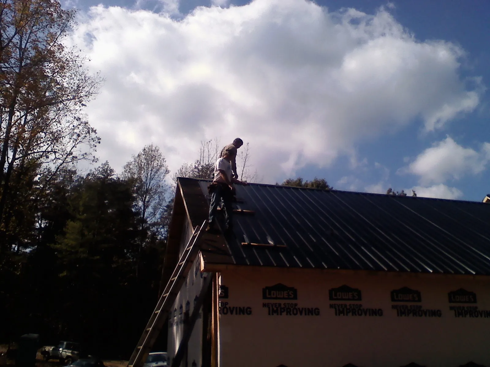 Roofer fastening dark metal panels high against a cloudy sky, from a Roof Inspection job in Showell
