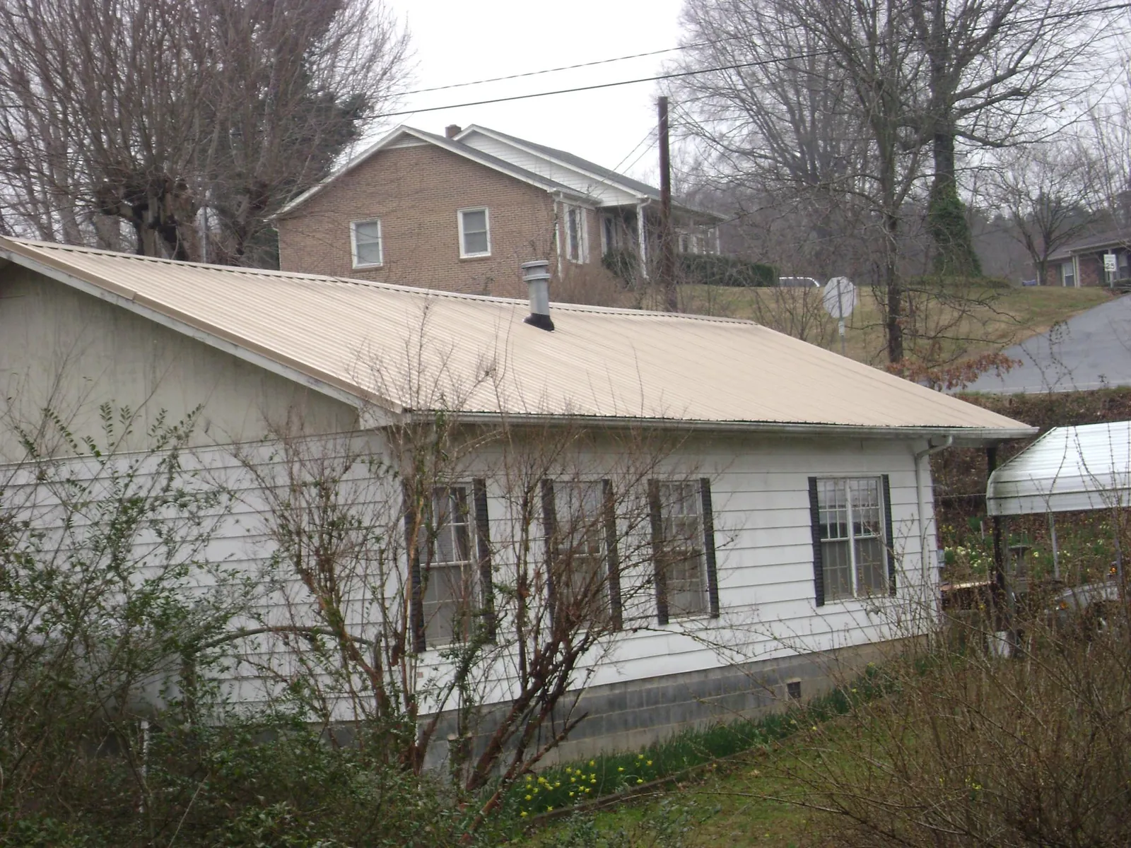 Tan metal roof on a white sided house set into a hillside — Commercial Roofing by Roofing Brothers in Showell